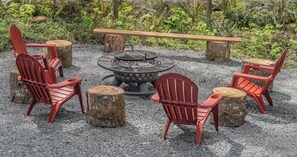 Un foyer entouré de chaises Adirondack rouges et d’un banc en bois.