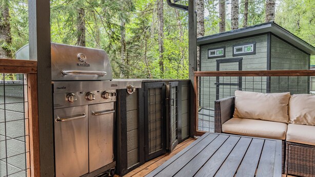 A covered outdoor area with a barbecue grill, a small shed, and a wicker sofa.