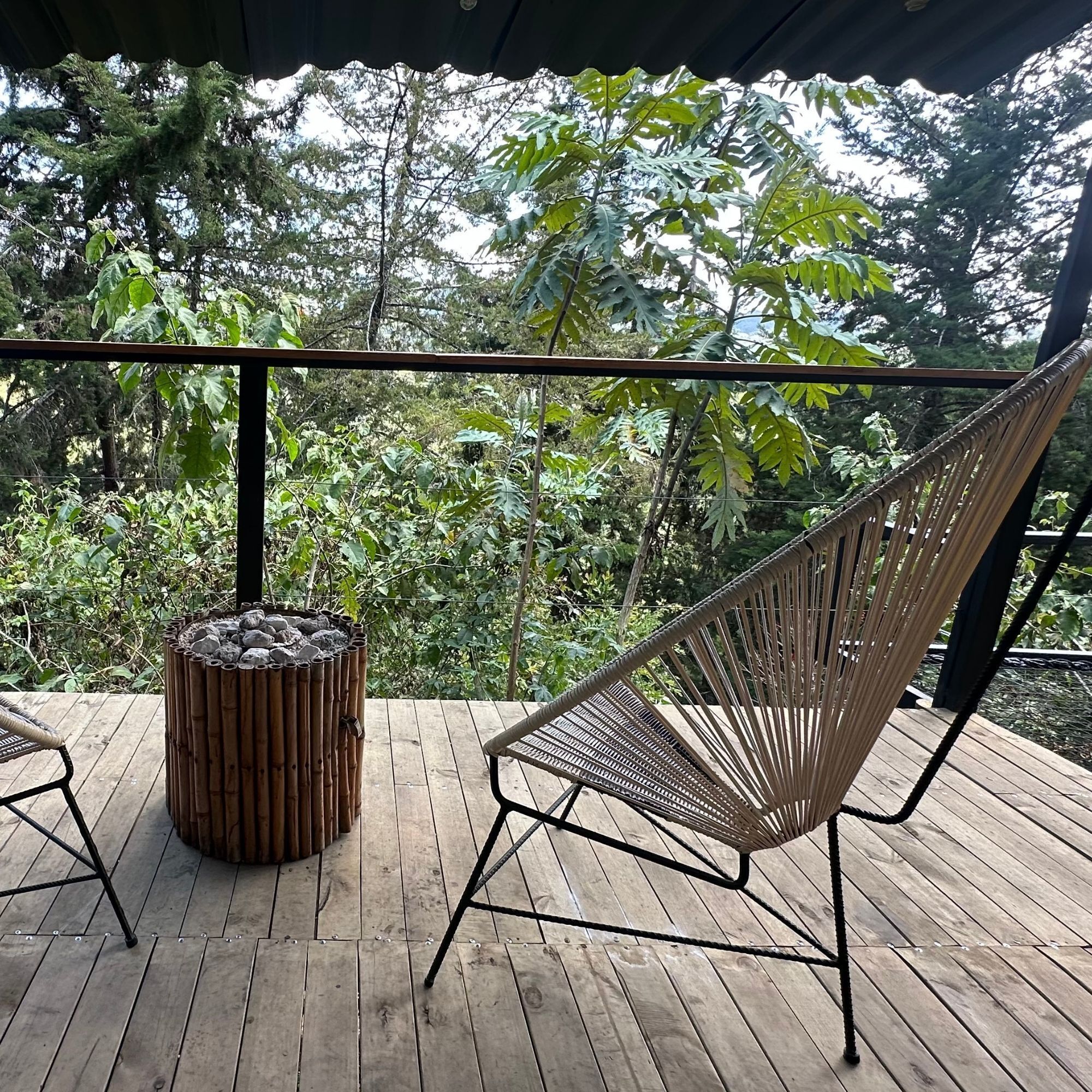 A wooden deck with a woven chair and a bamboo stool.