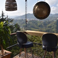 A terrace with two chairs, a hanging wicker lamp, and a large gong. The terrace overlooks a mountainous landscape with a view of a town in the distance.