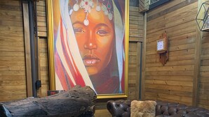 A room with a wooden floor, a large painting on the wall, a dark brown leather sofa with a fluffy pillow, and a rustic wooden bench. - Omghat (El Peñol)