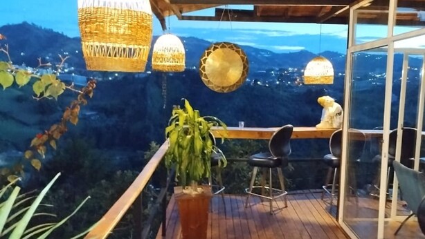 A wooden deck with wicker lamps and a view of a mountainous landscape. - Omghat (El Peñol)