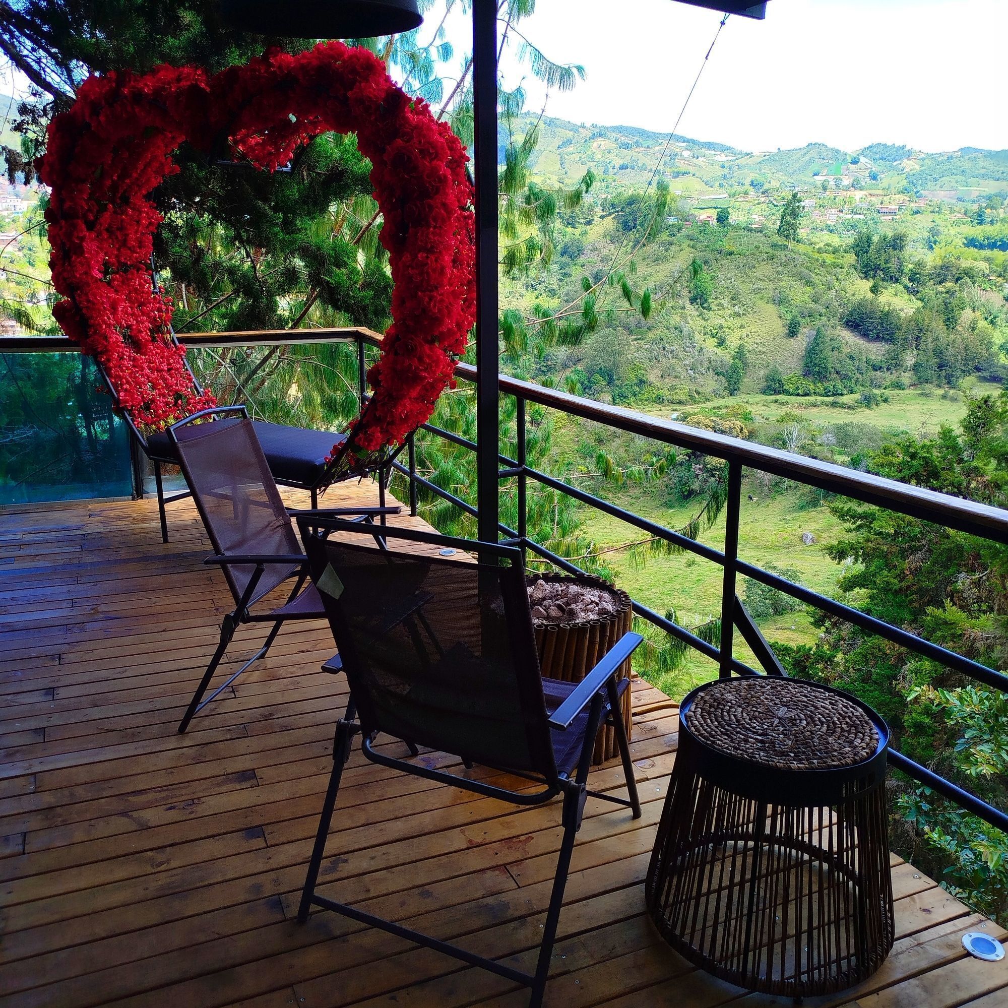 A wooden deck with outdoor seating, a heart-shaped floral decoration, and a view of a green landscape.