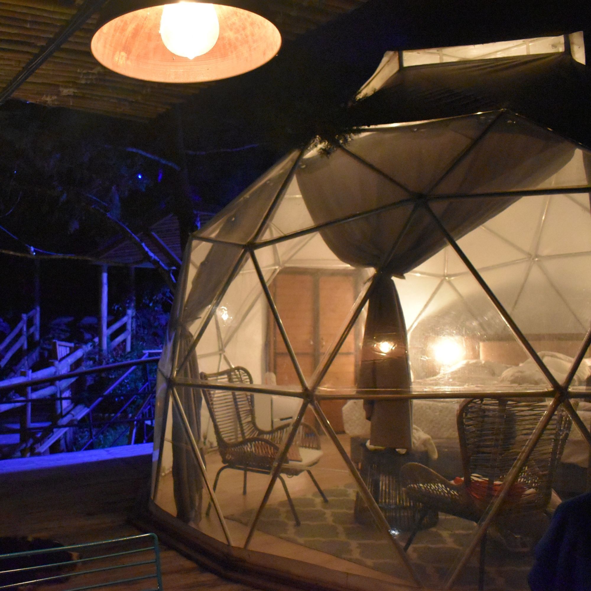 A geodesic dome structure with chairs inside, a staircase leading up, and a hanging light fixture.