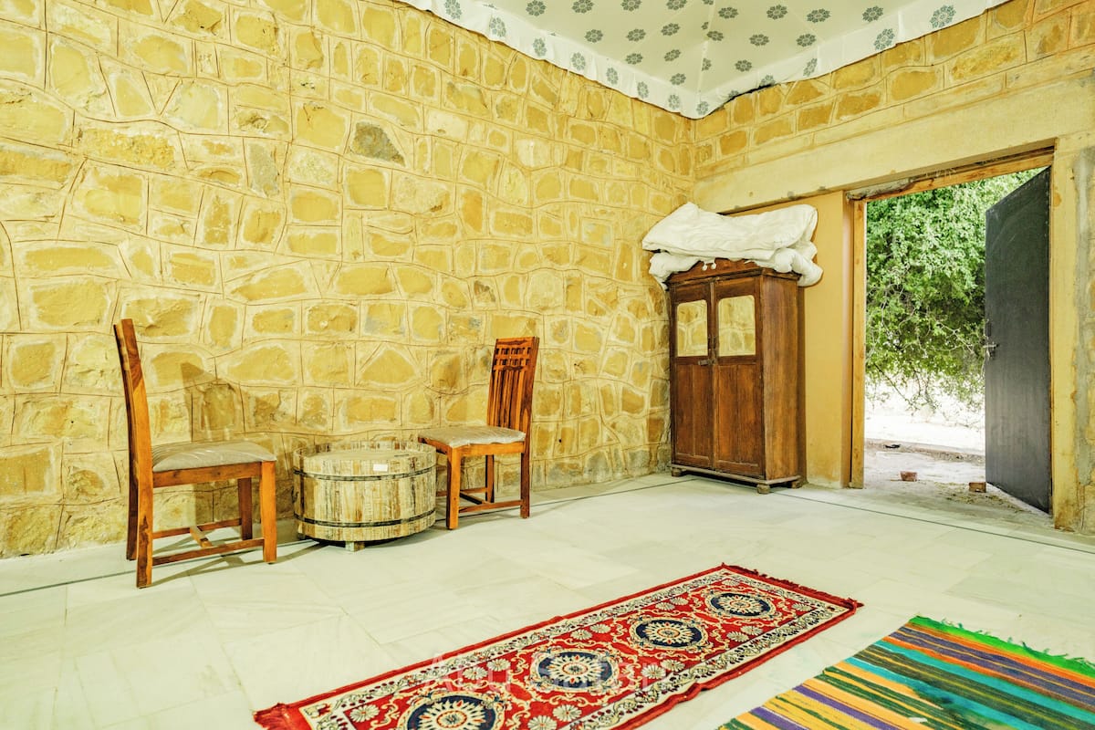 Una habitación con paredes de piedra, una puerta de madera, una silla de madera, un armario de madera y una alfombra colorida.