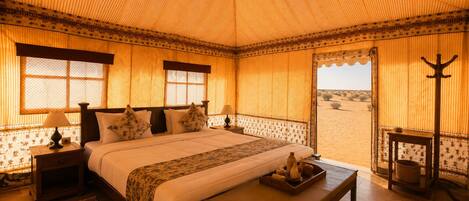 Habitación con una cama grande, una banca, una mesita de noche, una lámpara y vista al desierto.