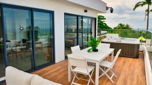 A modern outdoor patio with a dining table and chairs, a hot tub, and a glass-enclosed space with a view of the surrounding area. - Le Gaetana hôtel  (Sainte-Rose)