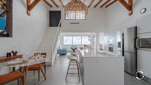 A modern kitchen with a central island, stainless steel appliances, and a staircase leading to a balcony. - Le Gaetana hôtel (Sainte-Rose)