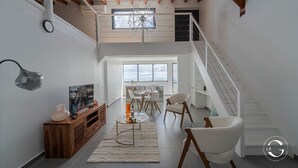 A modern interior with a staircase, a dining area, and a TV on a wooden console. - Le Gaetana hôtel (Sainte-Rose)