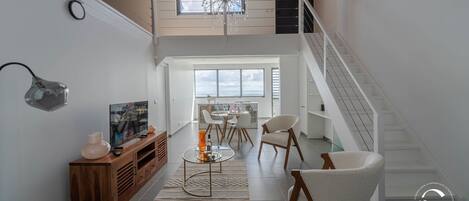 Un interior moderno con una escalera, un comedor y un televisor sobre un mueble de madera.