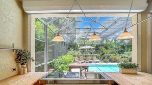 Eine Küche mit großem Fenster, Blick auf Pool und Garten.