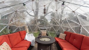 A geodesic dome structure with a central fire pit and red cushioned seating.