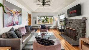 A modern living room with a leather sofa, a glass coffee table, a pink armchair, a fireplace, and a TV displaying 'NETFLIX'.