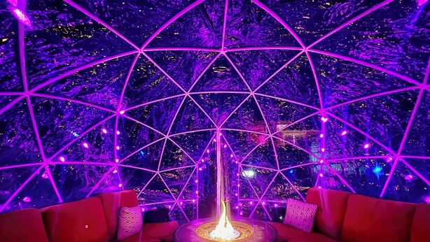 A room with a geometric ceiling design, a central fire feature, and red seating.