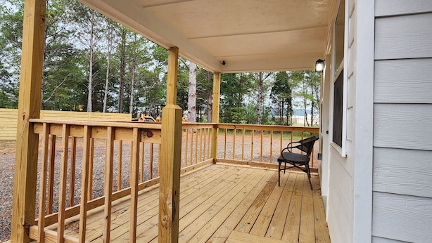 Eine Holzterrasse mit Geländer, einer Bank und Blick auf Bäume und ein Gewässer.