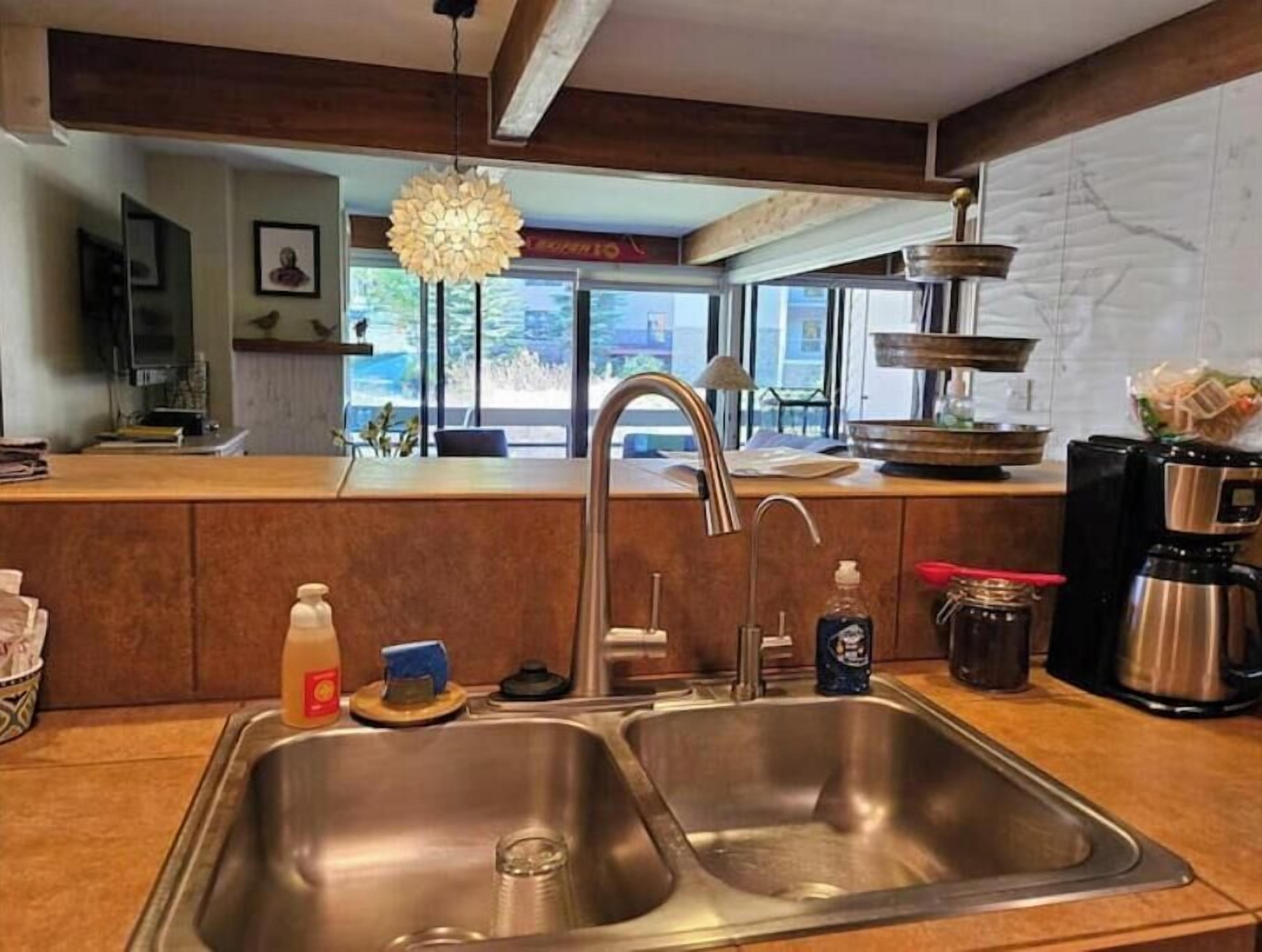 A modern kitchen with stainless steel sinks, a hanging light fixture, and a view of the outdoors.