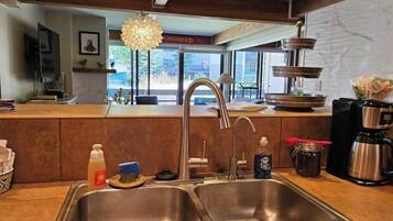 A modern kitchen with stainless steel sinks, a hanging light fixture, and a view of the outdoors.