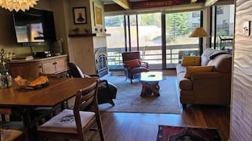 A cozy living room with a fireplace, a dining area with a wooden table and chairs, and a sofa.