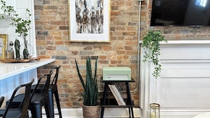 A modern living room with a brick wall, a mounted TV, a fireplace, and a dining area with black chairs and a white table.