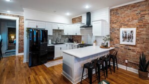 A modern kitchen with white cabinetry, a black refrigerator, and a brick accent wall.