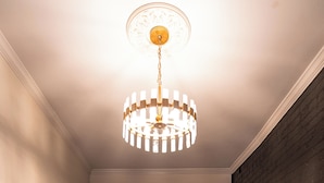 A room with a wooden floor, a black railing, a wall-mounted picture, and a hanging light fixture.