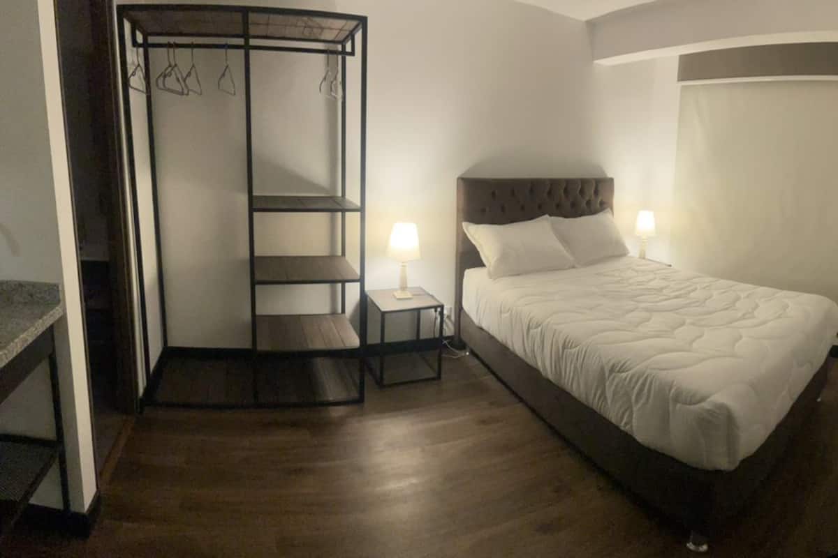 Una habitación de hotel con cama, mesita de noche, televisor, armario y una pequeña mesa con un florero.