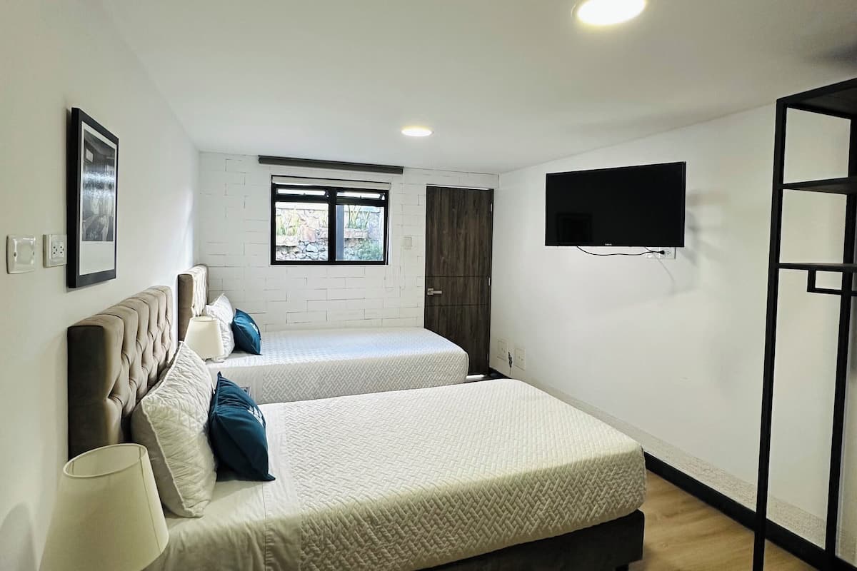 Un dormitorio con dos camas, televisión y ventana.