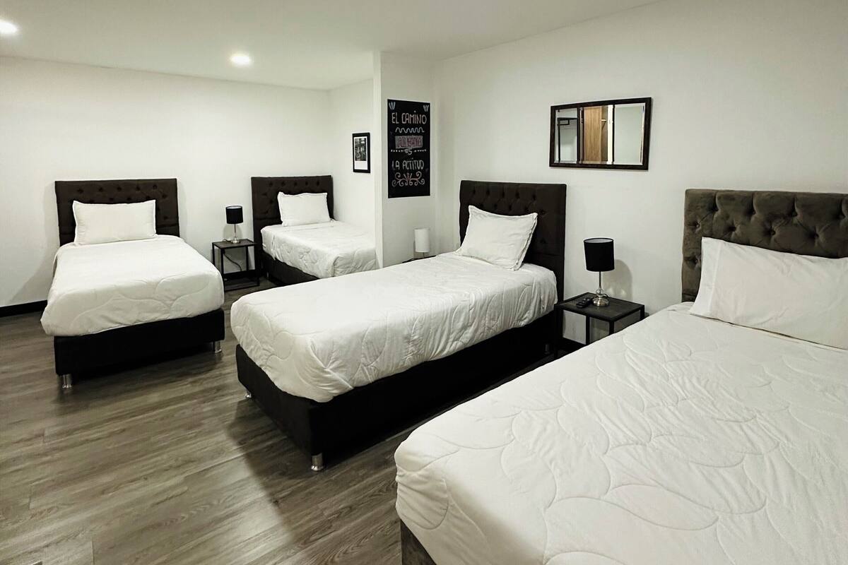 Habitación de hotel con tres camas, piso de madera y un espejo montado en la pared.