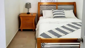 Une chambre à coucher comprenant un lit, une table de chevet, une lampe, un ventilateur de plafond et un appareil de climatisation.