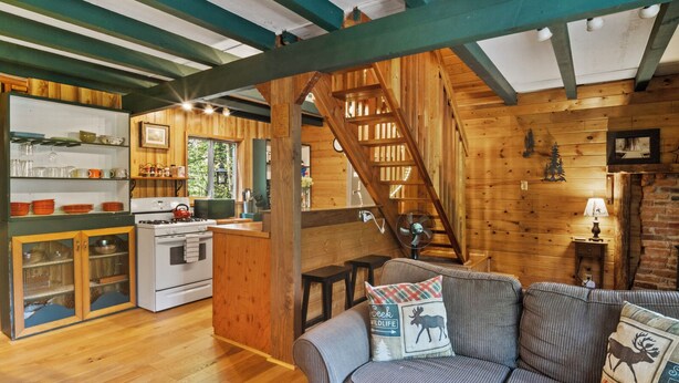 A cozy cabin interior with a kitchen, dining area, and a staircase leading to a loft. - Rainier's Iconic Cabin with Forest Views-WiFi-Hot Tub (Ashford)