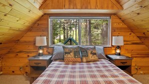 A cozy bedroom with a plaid bedspread, two bedside tables with lamps, and a window offering a forest view. - Rainier's Iconic Cabin with Forest Views-WiFi-Hot Tub (Ashford)