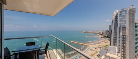 A balcony with a glass railing overlooking a beach and cityscape.