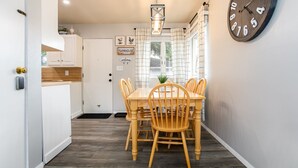 Un coin repas avec une table et des chaises en bois, une horloge au mur et une fenêtre avec des rideaux.