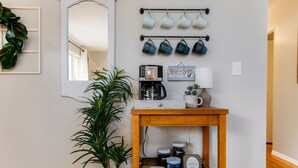 Une table basse en bois, avec une machine à café, des tasses et un panneau indiquant : « Réveillez-vous et profitez de la journée ».