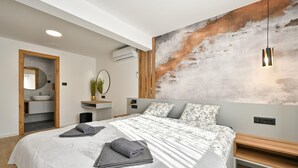 Ett modernt sovrum med en stor säng, ett träbord vid sängen, en väggmonterad luftkonditioneringsanläggning och en stor, abstrakt tavla.