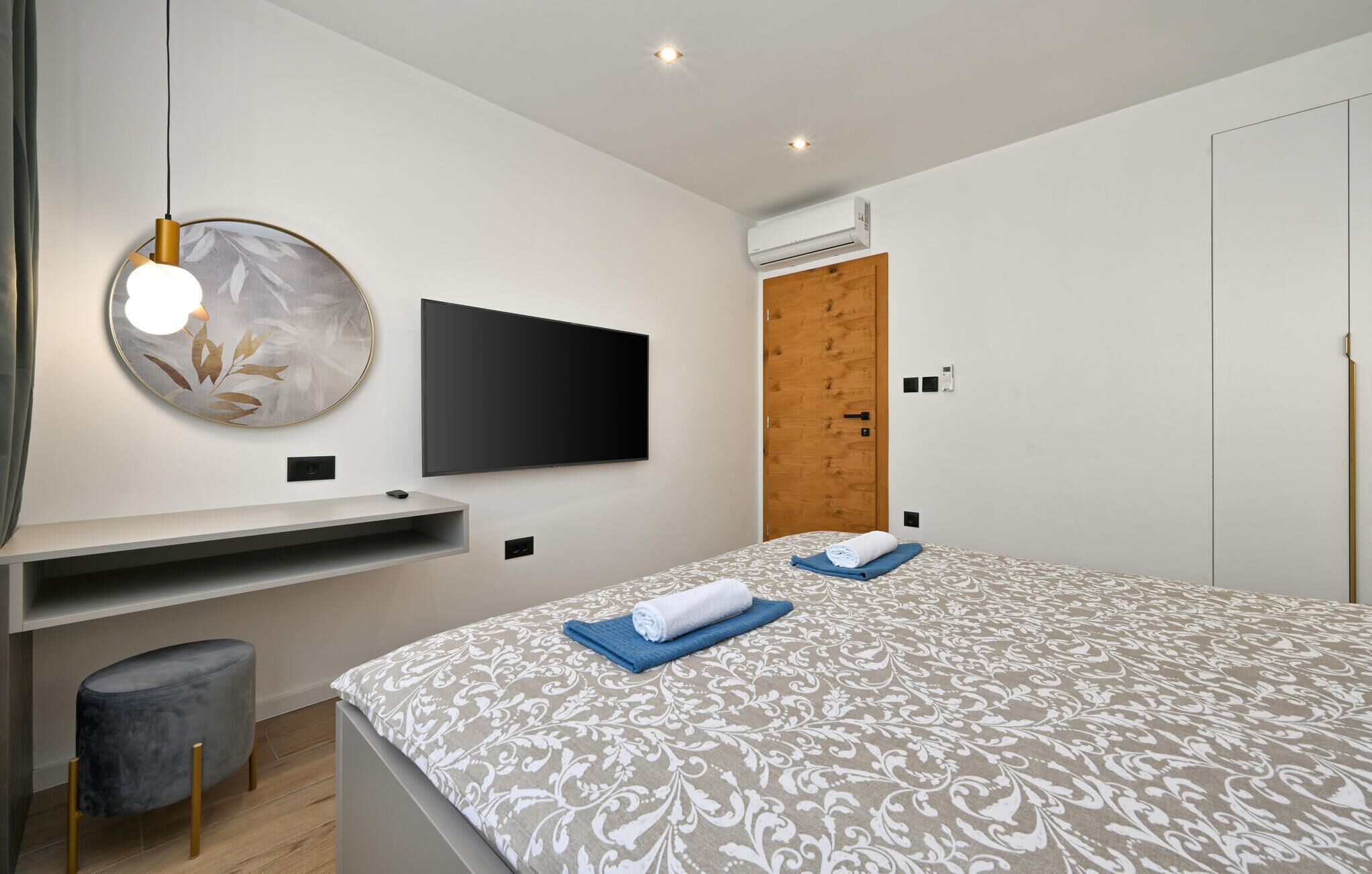 Une chambre moderne avec un lit, un téléviseur fixé au mur, un climatiseur mural et une porte en bois.