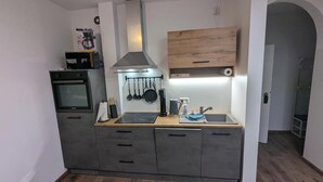 A compact kitchen with a built-in oven, a microwave, a stove, a wooden countertop, and a hanging pot rack.