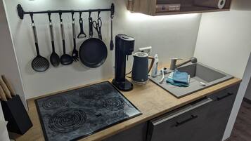 Une cuisine de taille réduite, équipée d’une cuisinière, d’un évier et de divers ustensiles.