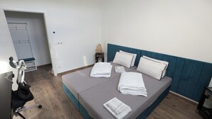 A neatly made bed with pillows and folded towels, a small bedside table with a vase, and a chair with wheels.