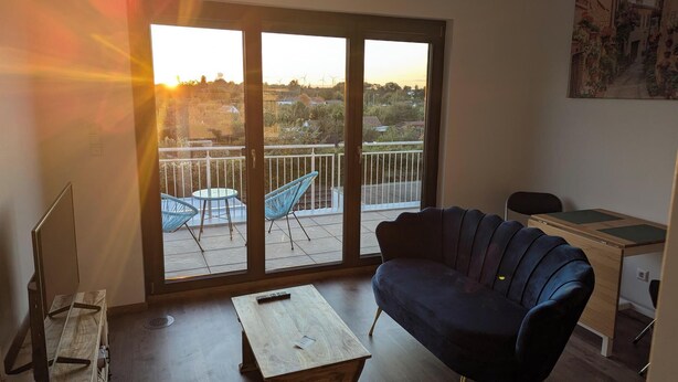A room with a balcony, a sofa, a small table, and a desk.
