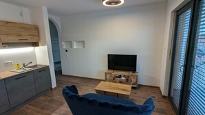 A modern living room with a flat-screen TV on a wooden stand, a blue sofa, and a wooden coffee table.