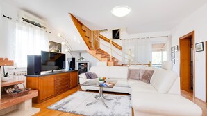 Una sala moderna con sofá, televisor, escalera de madera y un comedor con mesa y sillas.