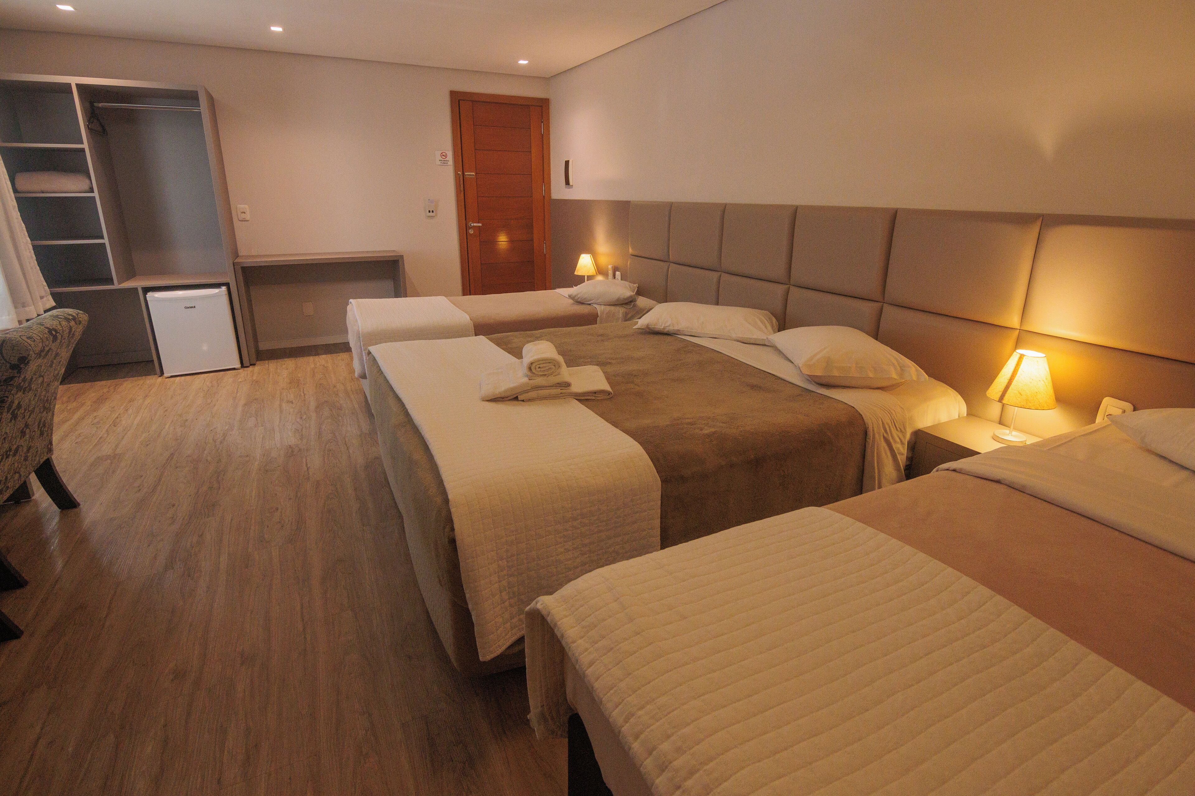 A hotel room with three beds, a wardrobe, a desk, and a small refrigerator.