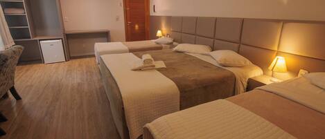 A hotel room with three beds, a wardrobe, a desk, and a small refrigerator.