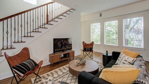 A spacious living room with a wooden staircase, a television, a sofa, and a coffee table. - Cozy retreat 5 Min from Downtown Houston 4bd - Rooftop Views !! (Houston)