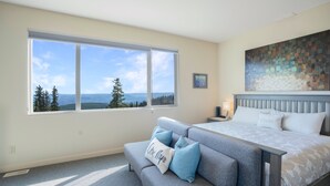 Ein Schlafzimmer mit großem Fenster, einem Bett, einem grauen Sofa und einem Deckenventilator.