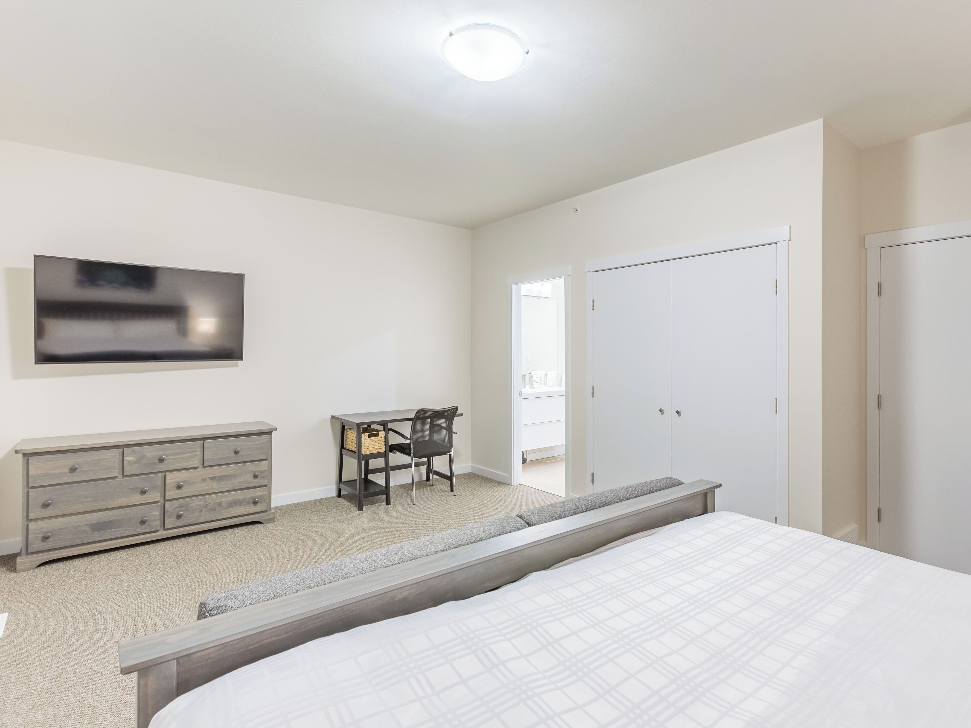 A bedroom with a bed, a dresser, a desk with a chair, a TV, and a wardrobe.