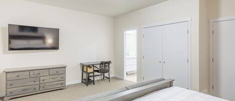 A bedroom with a bed, a dresser, a desk with a chair, a TV, and a wardrobe.