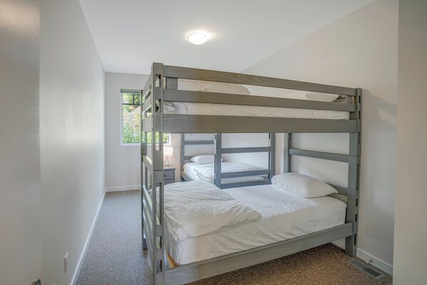 Una cama litera con ropa blanca en una habitación con paredes blancas y una ventana.