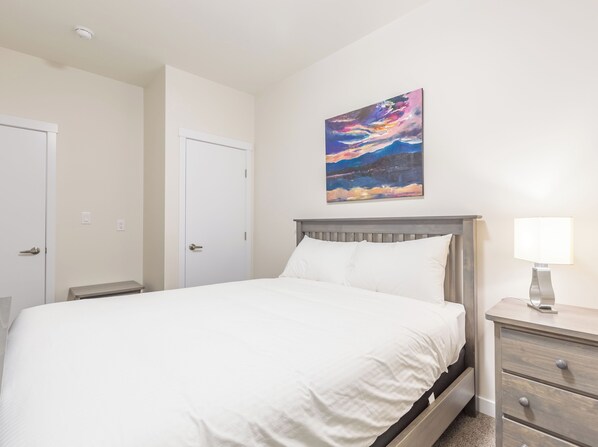 A hotel room with a bed, a nightstand, a lamp, and a painting on the wall.